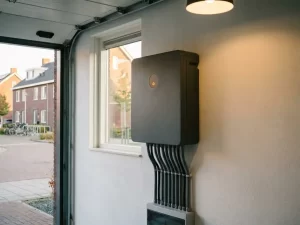 Thuisbatterij op witte garagemuur met amberkleurig lampje en netjes weggewerkte kabels in Nederlandse woning.