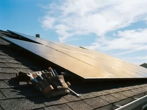 Zonnepanelen op hellend woonhuisdak glanzen in middagzon, met gereedschapsriem op dakrand en heldere blauwe lucht op de achtergrond.