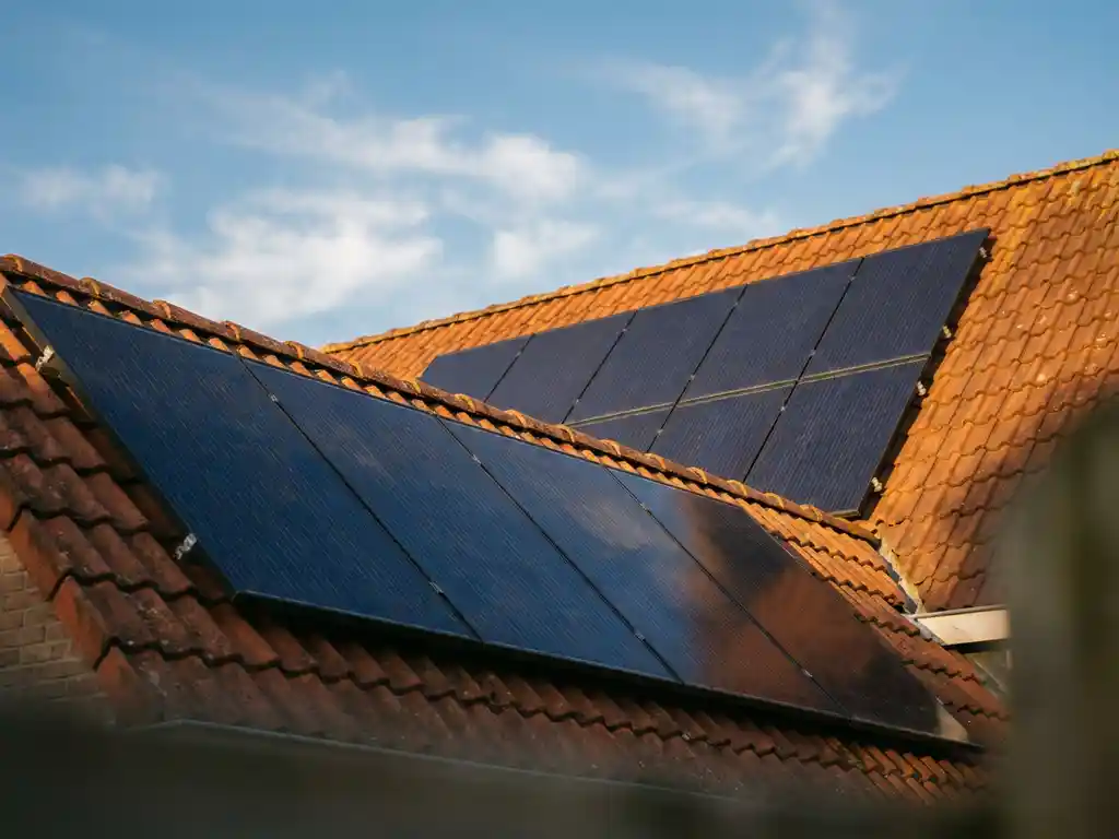 Acht zonnepanelen op een Nederlands woonhuisdak in warm middaglicht, omringd door terracotta dakpannen en een blauwe lucht.