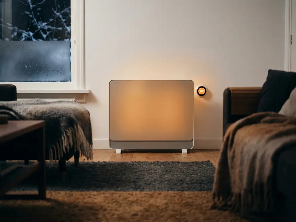 Elektrische paneelverwarming aan witte woonkamermuur met warme gloed, houten vloer en slimme thermostaat in Nederlands interieur.